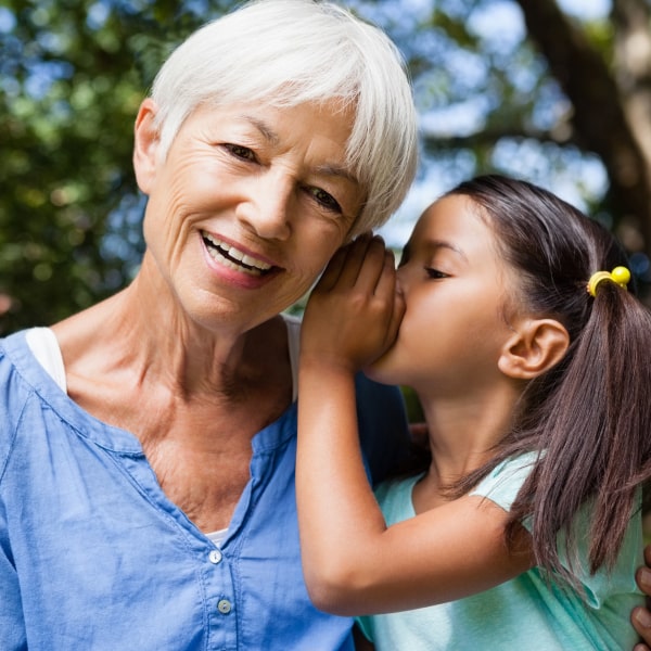 Image of an elderly woman and a little girl whispering something in the woman's ear